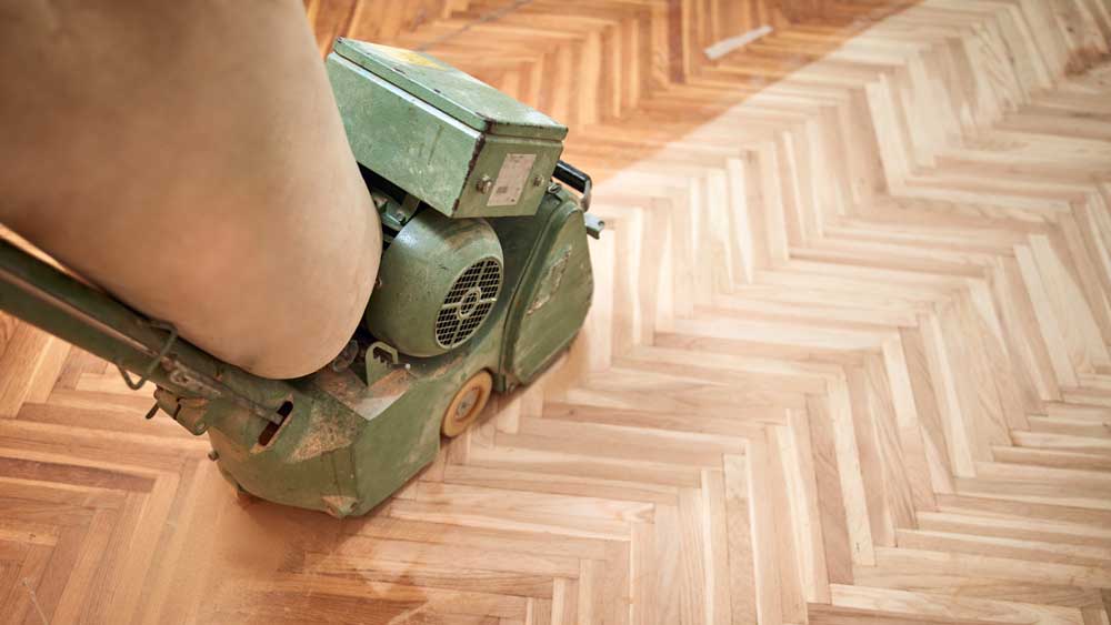 Hardwood floor sanding machine restoring a herringbone wood floor
